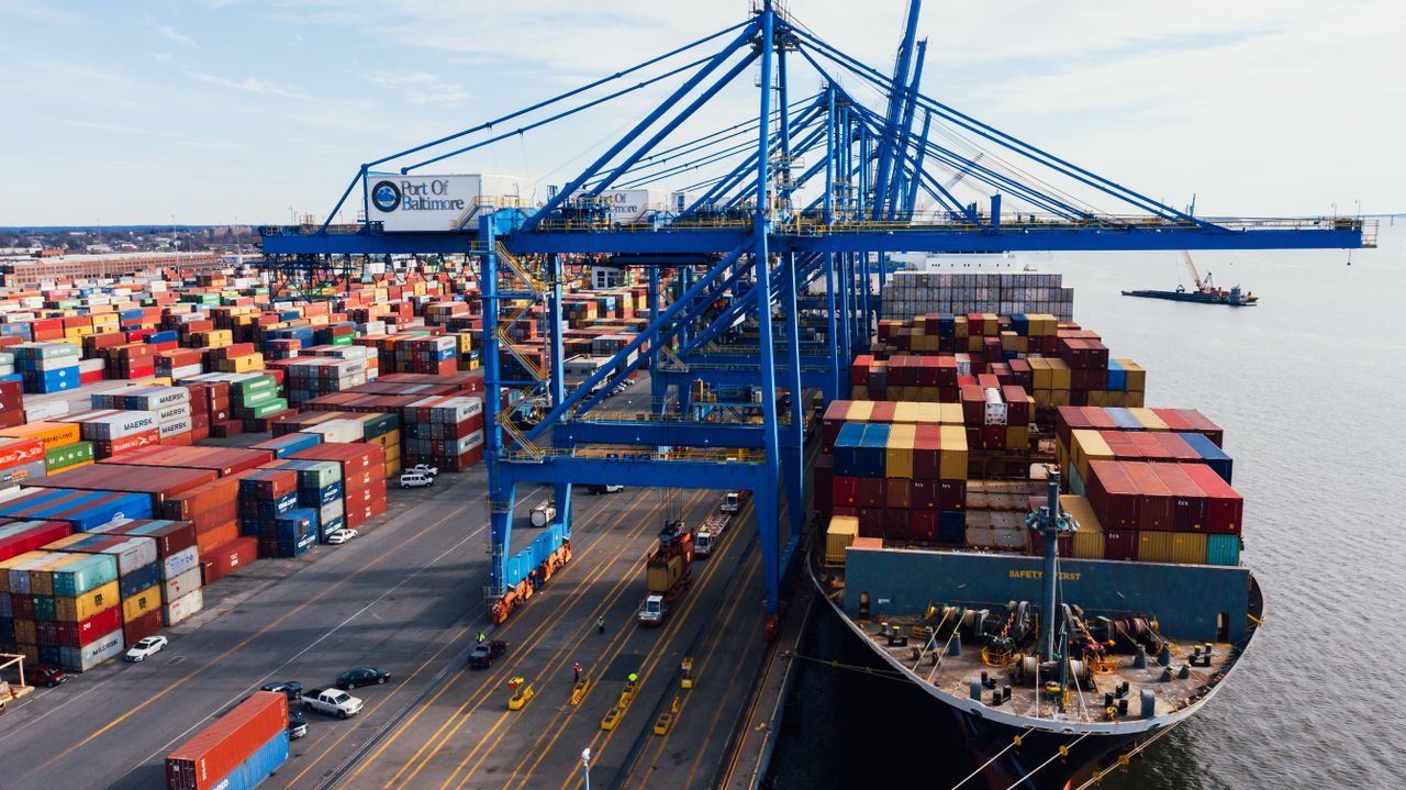 High angle of huge cargo vessel moored in industrial port and loading colorful containers in cloudy day
